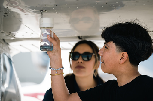 The flight instructor hands over the fuel quality tester to her student.