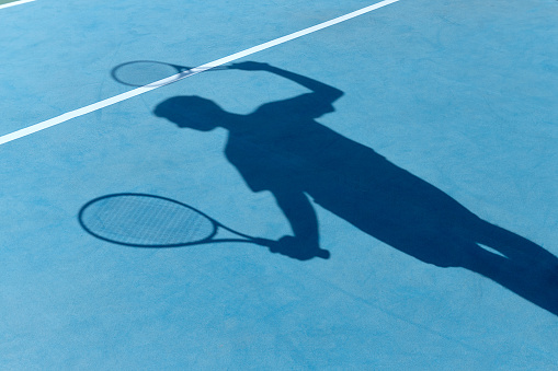 Vintage tennis racket with a ball on the tennis court. Shadow of tennis players on tennis court.