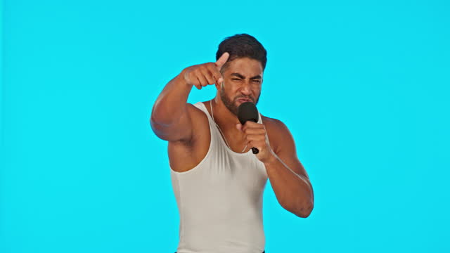 Singer, rapper and man dancing with microphone in studio to sing or rap on blue background. Happy male model, artist or musician dance for hip hop music performance for a live concert or event