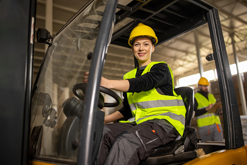 Mid adult Caucasian woman driving a forklift in a warehouse
