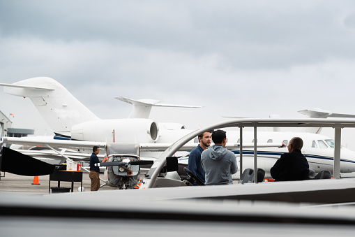 Several people are sitting comfortably on a golf cart, chatting away, while an engineer is conducting aircraft inspections in the background.