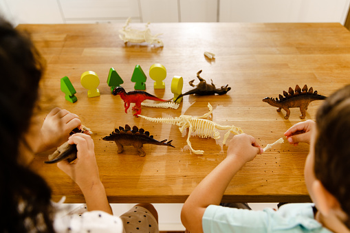 Above shot of Children having fun playing with dinosaur toy on the kitchen island