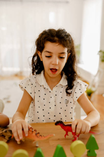 Little gurl playing with dinosaur toys on the table at home