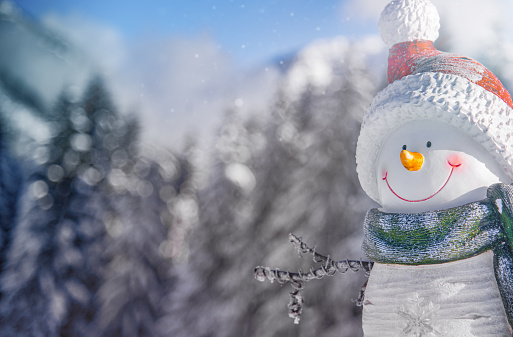 Small cute snowman with gift in fir forest under falling snow