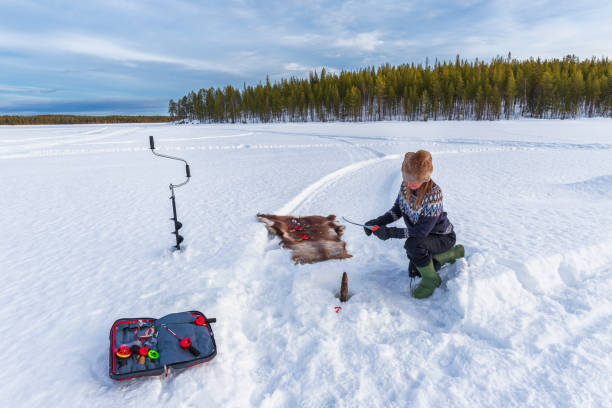 Winter fishing through the ice on a frozen lake Woman caught fish while ice fishing in the winter ice fishing stock pictures, royalty-free photos & images