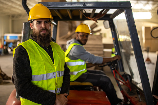 Portrait of two young warehouse workers, one in a forklift