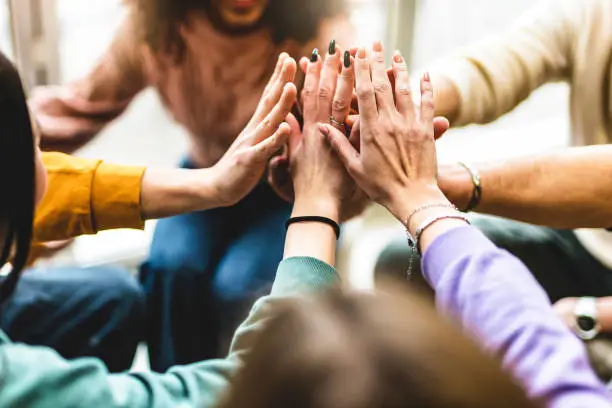 Photo of Young multiracial group stacking hands together- Happy diverse friends united at community table having fun- youth Millennial students giving strength motivation- Human resources teamwork concept