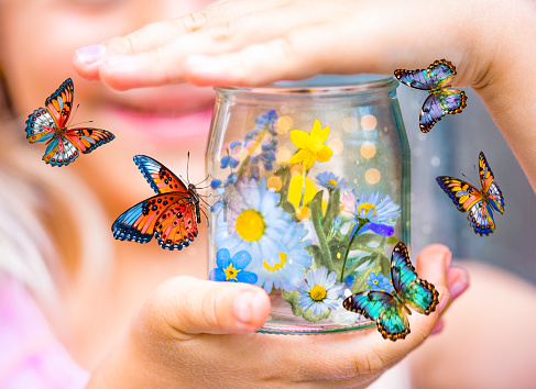Girl Holding a Glass Jar with Wildflowers in It. Butterflies Flying Around the Jar