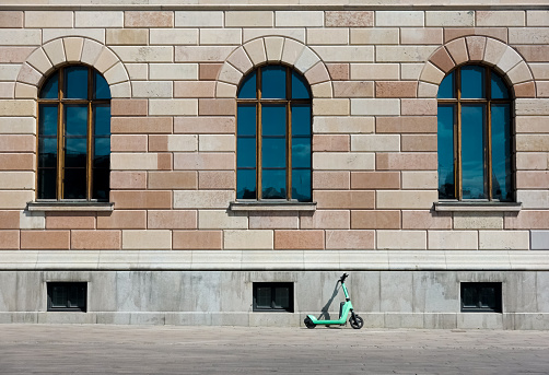 Modern electric scooter leaning on facade of historic stone building as a contrast of old and new