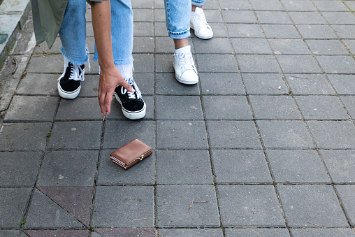 Two women pedestrians find a lost wallet on the sidewalk in a pedestrian zone on a street in the city someone has dropped it from their pocket or purse and the girl reaches out to pick it up and return it to its owner.