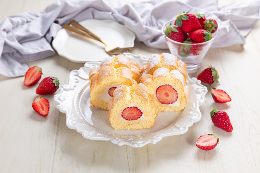 Cake roll with strawberries and cream cheese on a white wood background