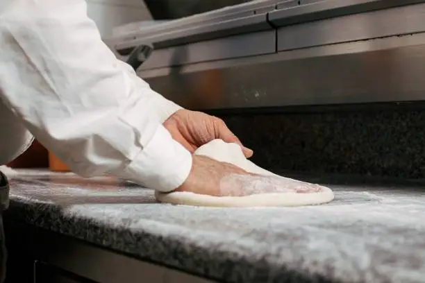A chef is skillfully making pizza dough on a marble kitchen countertop