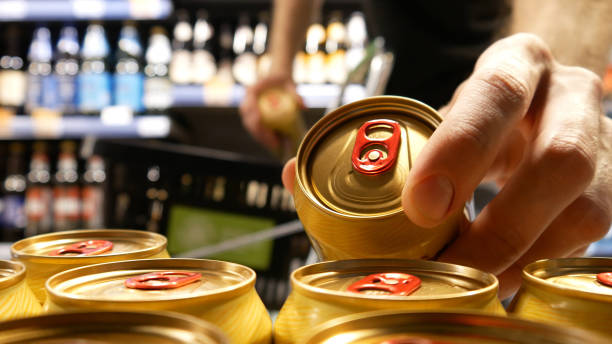 Close-up of a buyer hands taking two beautiful golden cans of beer and putting them into a shopping trolley stock photo
