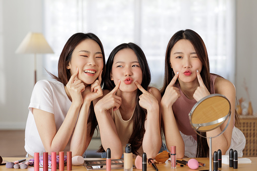Three Asian models exude happiness and confidence as showcase radiant skin. With radiant smiles and fingers delicately placed on cheeks, they highlight their flawless complexions.