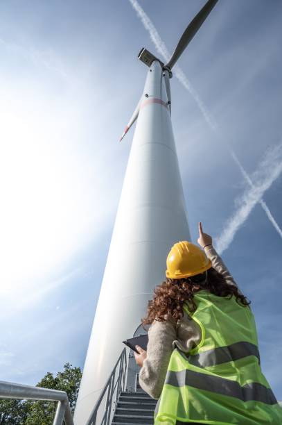 istock Female professional wearing a hard hat standing and pointing to a windmill 1496122139