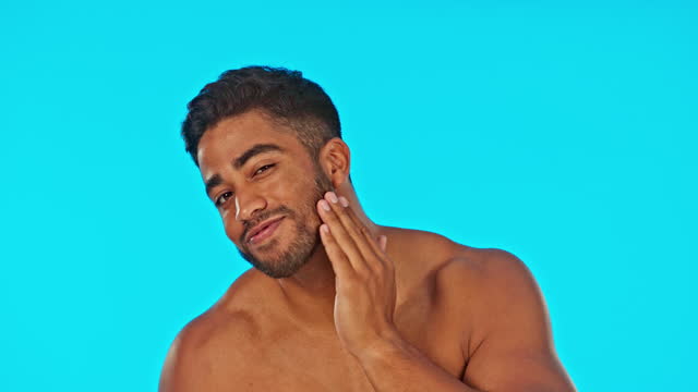 Face, skincare smile and man with serum in studio isolated on a blue background. Hair care, dermatology cosmetics and happy Indian male model with hyaluronic acid, retinol or essential oil for beard.