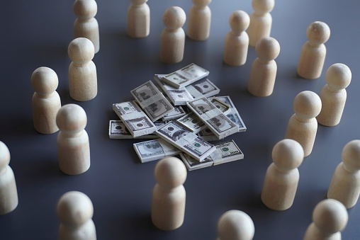 Group of wooden dolls and stack of money. Finance, donation, investor and crowdfunding concept