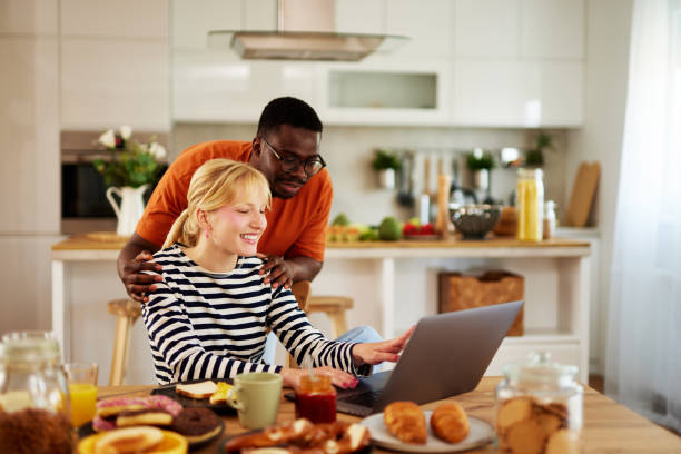istock Young multiracial couple talking and using a laptop over breakfast at home 1496124682
