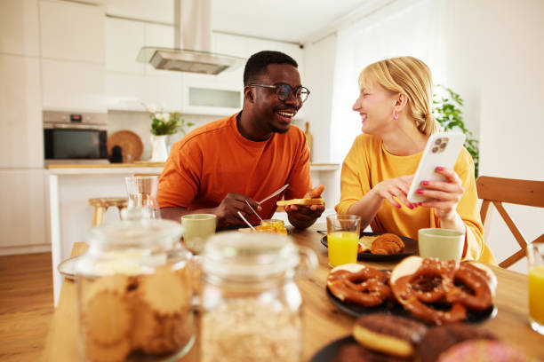 istock Happy multiracial couple using mobile phone together over breakfast at home 1496126034