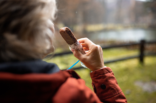 One woman, mature female enjoying a chocolate bar on autumn day outdoors.