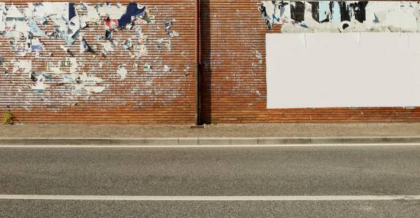 Grunge brick wall covered with ripped billboards except one blank on the right.  Sidewalk and urban street in front.