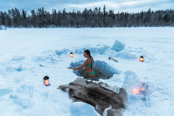 Woman enjoys ice bath, Lapland View of a beautiful woman ice bathing in the hole of a frozen lake surrounded by the arctic forest, Sweden swedish sauna stock pictures, royalty-free photos & images