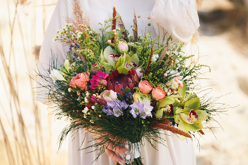 Wedding bouquet with eustoma, orchids, bellflowers, peonies and wildflowers in boho style on a bright background
