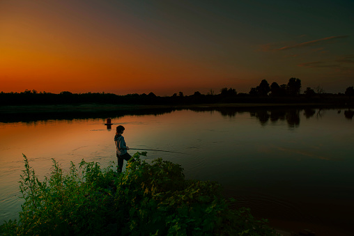 A fishing girl at sunset, against the background of an incredible landscape. A big river. serenity and silence, alone with nature. the concept of outdoor sports recreation. fishing and tourism