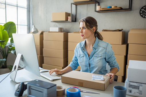 Frustrated young woman in yellow sweater standing at table and touching face with hand while packing stuff in office after dismissal