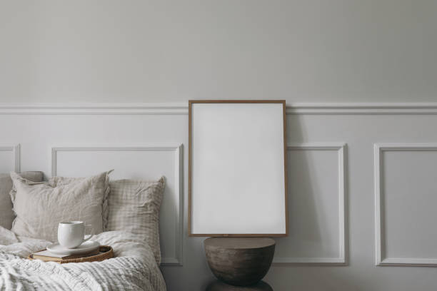 istock Elegant boho bedroom interior. Vertical wooden picture frame mockup on modern organic shaped side table. Cup of coffee on tray. Breakfast in bed concept. Beige linen throw. White wall background. 1496140604
