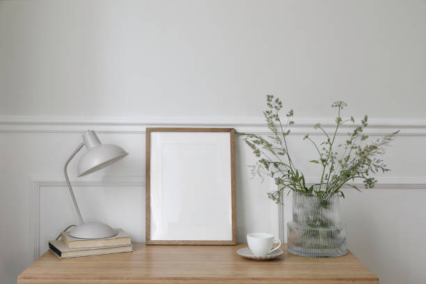 istock Elegant working space, home office. Cup of coffee, lamp, books. Empty vertical picture frame mockup on wooden desk, table. Vase with green grasses and cow parsley. Scandinavian interior design. 1496140713
