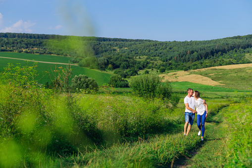 beautiful sunny day. meadow with green grass and forest. couple in love walking and kissing.