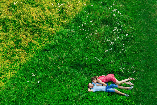 couple in love laying on the green field on summer day. top view from drone