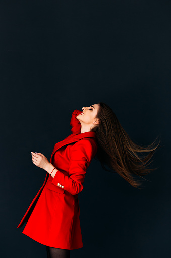 Young gorgeous model in red coat throwing her hair on dark background