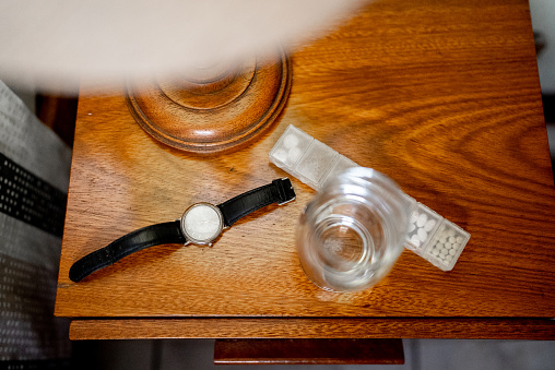 Bedside table with a wristwatch, pills and glass of water