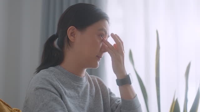 Asian woman was sick with sore eyes sitting on armchair in living room at home.