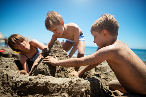 Little boys and their sister are having fun on beach. Kids are building sandcastles.\nAndalusia, Costa del Sol, Spain . Children are aged 7 and 11.