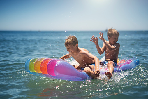 Two little boys are having fun on pool raft floating on the sea. Kids splashing and swimming fast.\nNikon D810