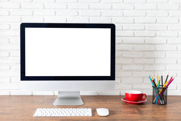 istock Mockup blank screen computer on a wooden desk. desktop empty white screen, with workspace and office supplies on table 1496153068