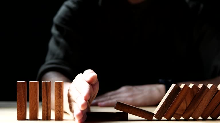 Close up Businessman hand stopping wooden domino business crisis effect or risk protection on dark background. Concept of Risk, Management, Assessment, Business, Crisis, Financial, Planning, Economic