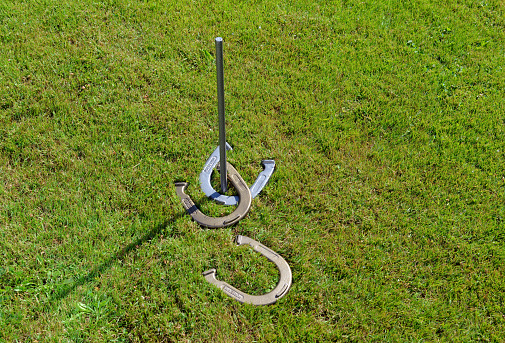 Closeup of a generic horseshoes game on a lawn in the sunshine.