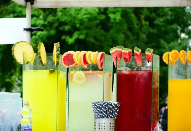 cold drink street vendor closeup view. glass flavored drink container. fruit juice. pineapple, grapefruit and watermelon slices along the glass edge.  selective focus. blurred background. summer scene