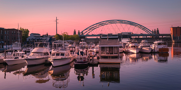 Sunset over the tranquil Providence River with arching highway bridge, moored boats, and water reflection in Rhode Island