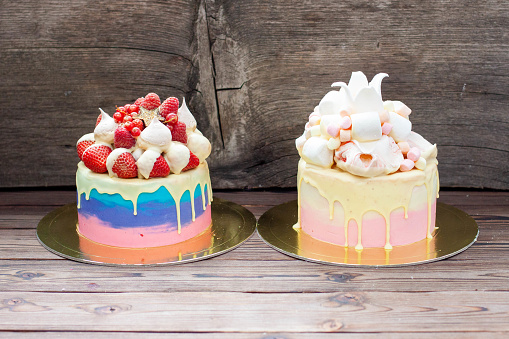 Two colorful cakes. The pink and blue one with melted white chocolate, fresh strawberry and raspberry. The pink and white one with fondant crown