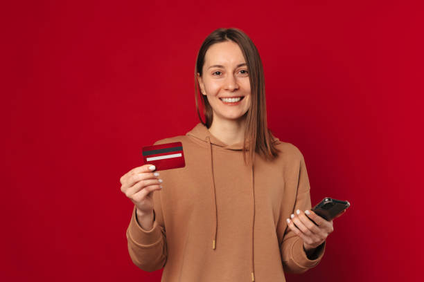 Cheerful woman is using mobile banking while holding her phone and card. stock photo