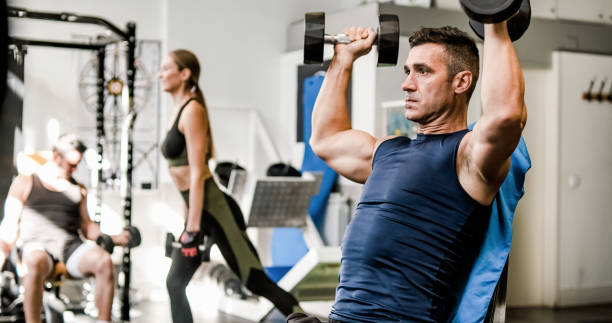 Muscular man exercising with dumbbells in gym stock photo