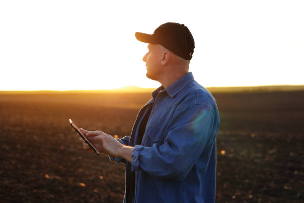 istock Smart farming technology and agriculture. Farmer uses digital tablet on field with plowed soil at sunset. Checking and control of soil quality, land readiness for sowing crops and planting vegetables 1496164925