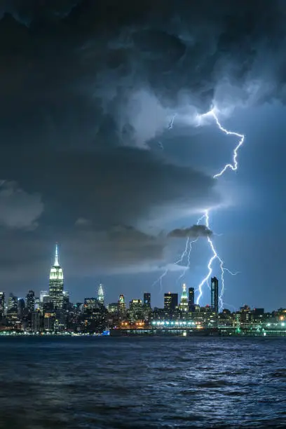 Photo of Lightning striking Midtown New York City skyscrapers at night. Stormy skies over Manhattan from the Hudson River
