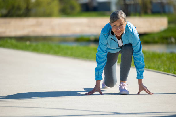 Beautiful young woman athlete preparing for running on the path through the wood simulating the starting position from the block. Healthy lifestyle, endurance for marathon training and cardio workout in the morning.