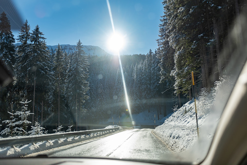 Firs Covered by the Snow in Apls Mountains in the North of Italy in Winter taken by the inside of a Car with Sunflare. Concept of Travels for Vacation in Winter